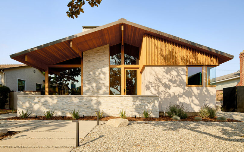 A modern single-story house with a slanted, overhanging roof, large windows, and a desert landscape garden featuring succulents and rocks.