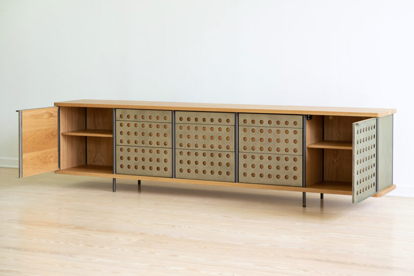 A long, modern sideboard with a light wood finish and perforated doors, standing on slim metal legs.