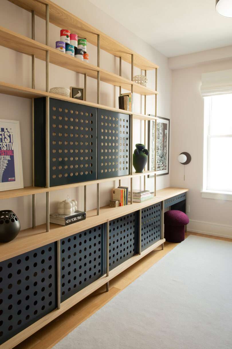 Modern room with light wood shelving featuring black perforated panel cabinets, books, decor, and framed art pieces.