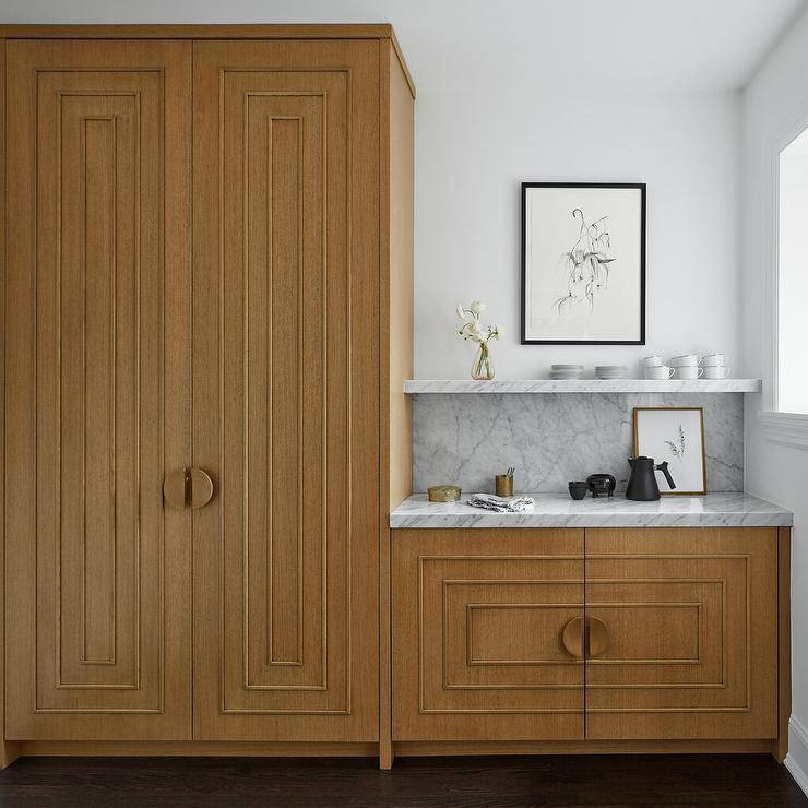 Chic pantry features gold, art deco style cabinets adorned with half moon, brass hardware. A marble backsplash and shelf sits over a coffee station.