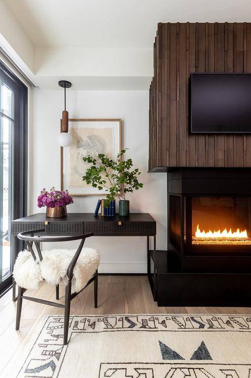 Black desk with black wishbone chair sits next to vintage style fireplace.