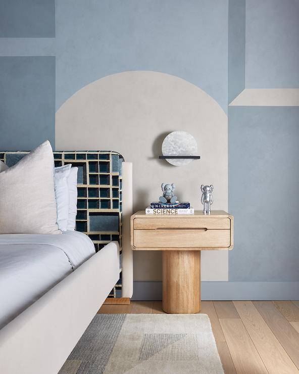 A charming white and blue wall is fixed behind a pedestal nightstand placed beside a vintage style bed positioned on a white and blue rug.