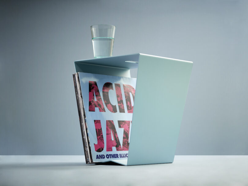 blue aluminum side table with a glass of water placed on top and vinyl records stored inside