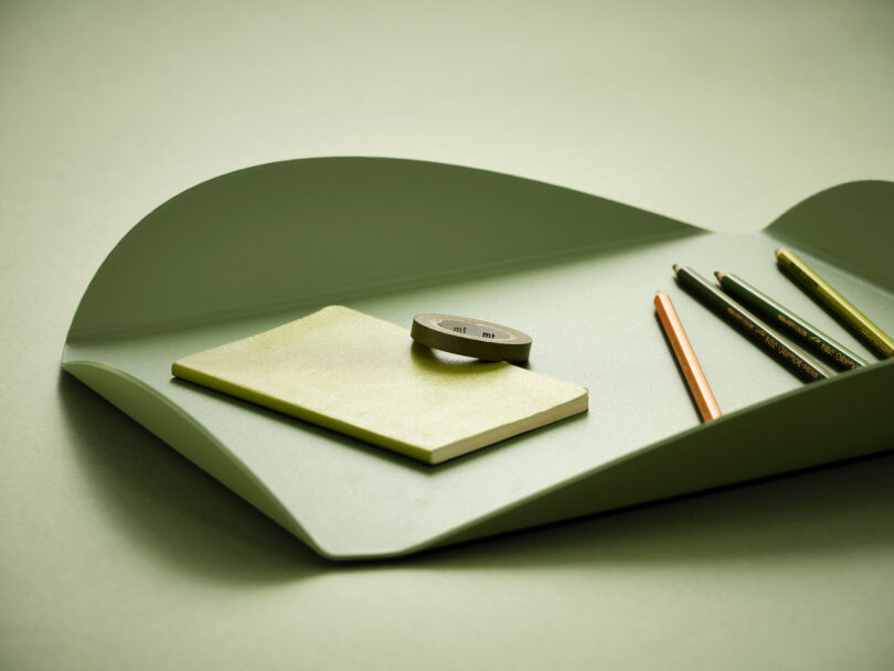 green tray with pencils, tape, and notebook placed inside