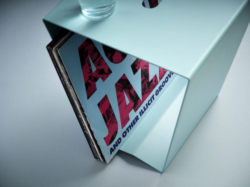 blue aluminum side table with a glass of water placed on top and vinyl records stored inside