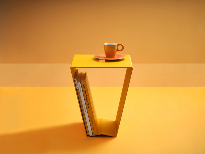 orange aluminum side table with a cup of coffee placed on top and books stored inside