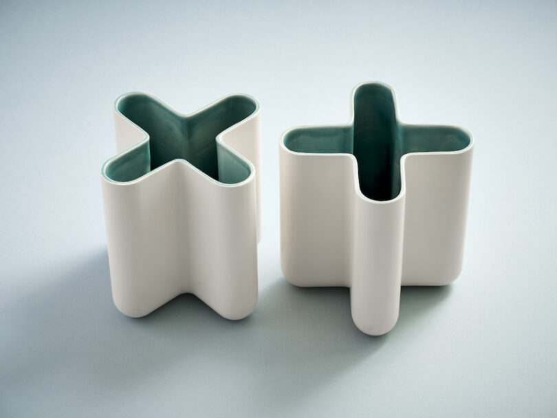 two white x-shaped vases on a teal background