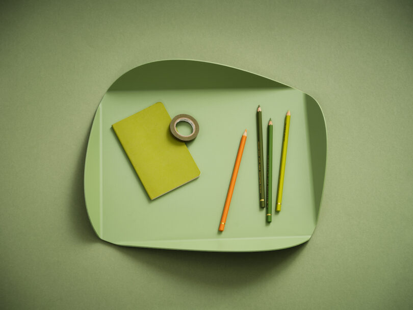 green tray with pencils, tape, and notebook placed inside