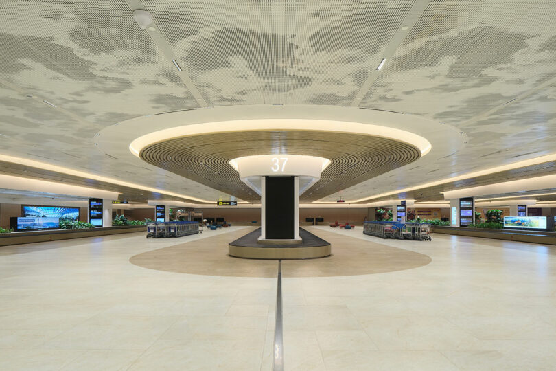 Modern airport baggage claim area with circular ceiling design and carousel number 37 in the center.