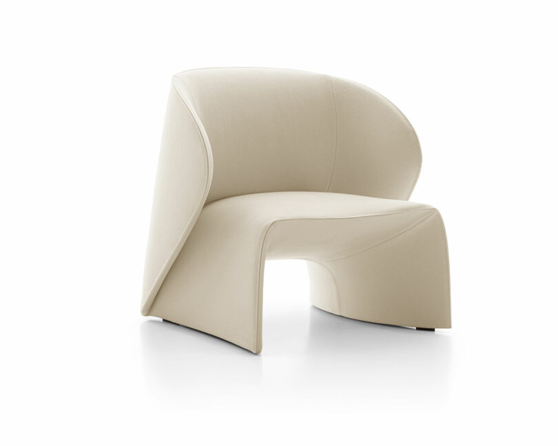 A modern, beige fabric lounge chair with a rounded, open back and smooth, curved lines. It sits on a white background.