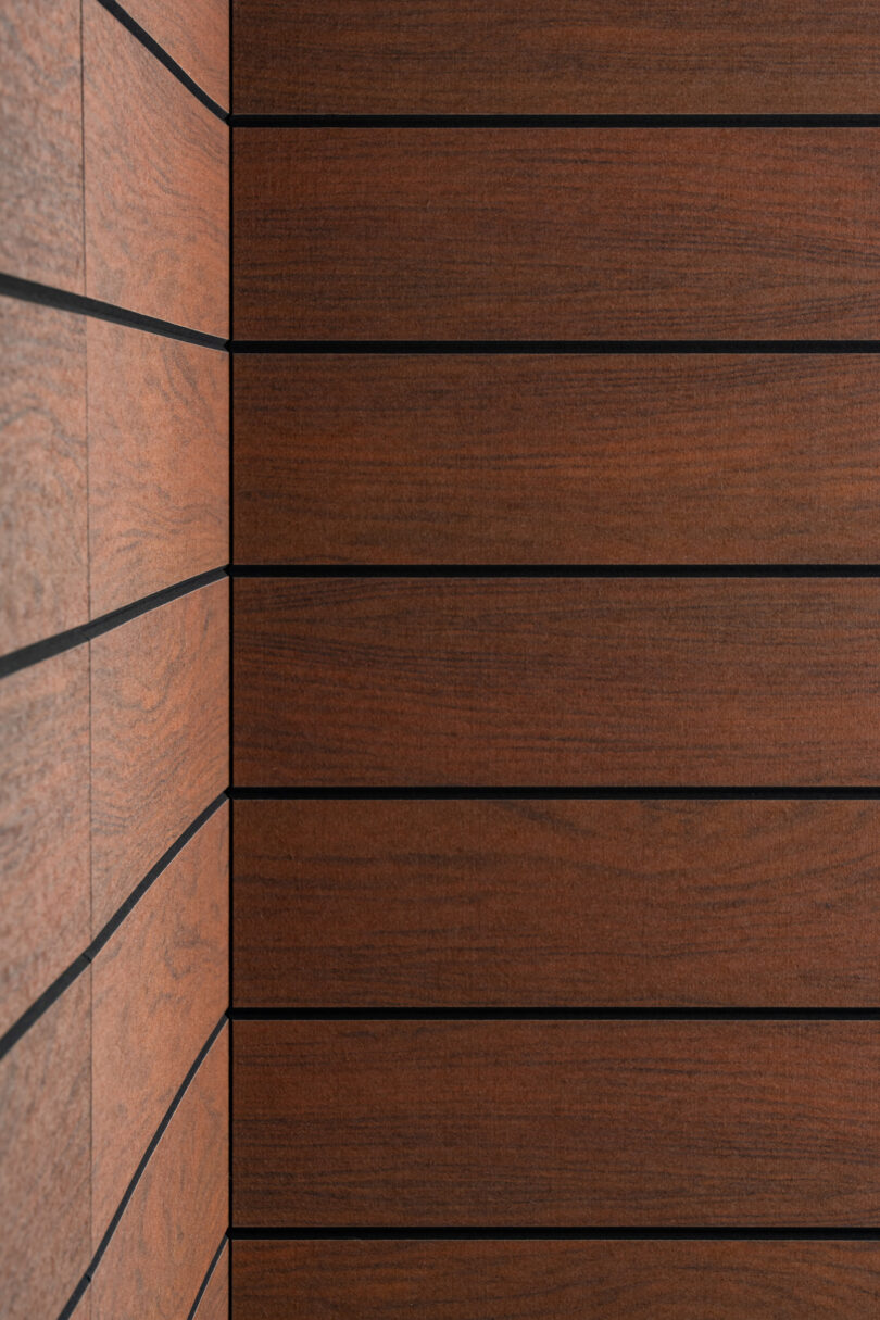 A corner of a wall composed of horizontal wooden panels with dark lines separating each panel. The left side shows two intersecting walls forming the corner