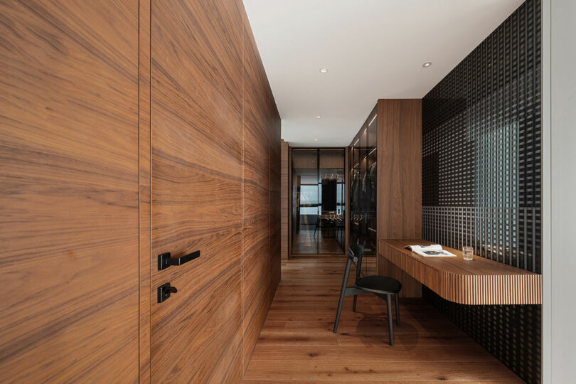 A modern hallway features wooden walls and floor, a built-in desk with a chair, and a wardrobe with glass doors on the right side.