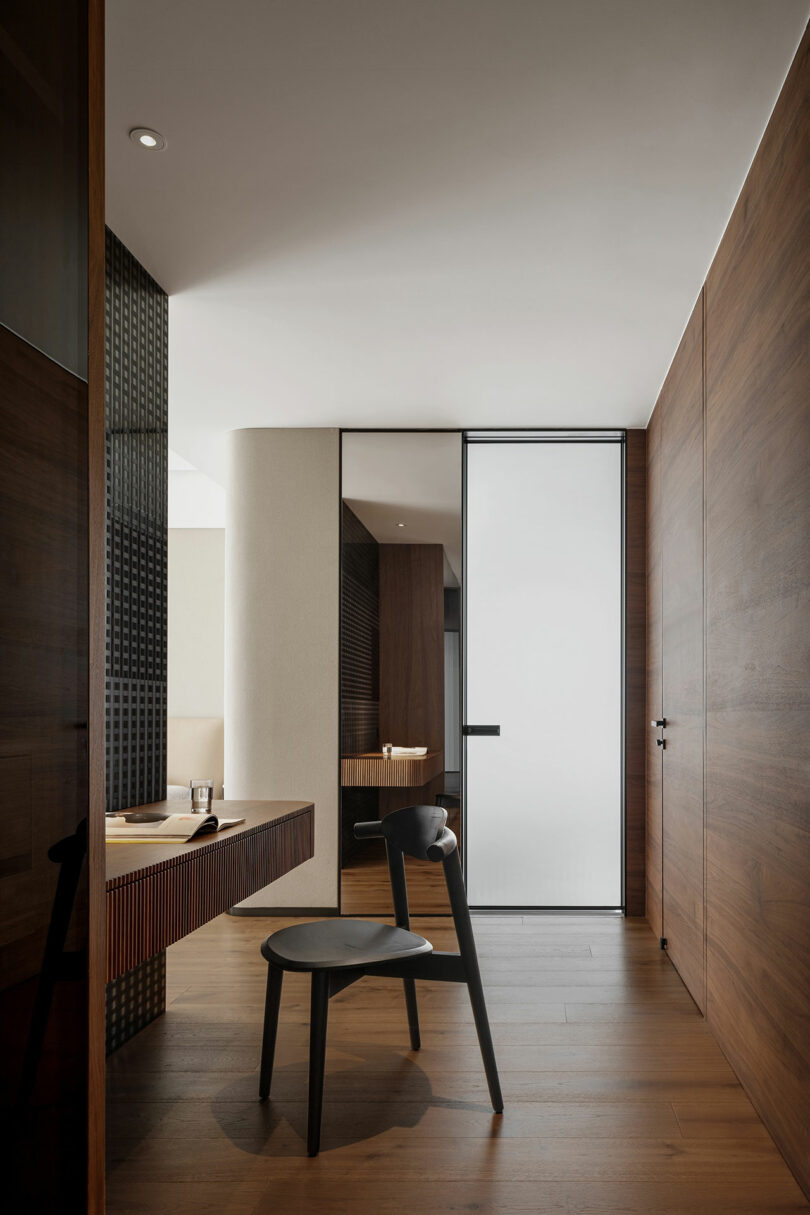 Minimalist room with wooden floors and walls, featuring a simple desk, chair, and a frosted glass door. A soft light illuminates the space, creating a serene atmosphere.