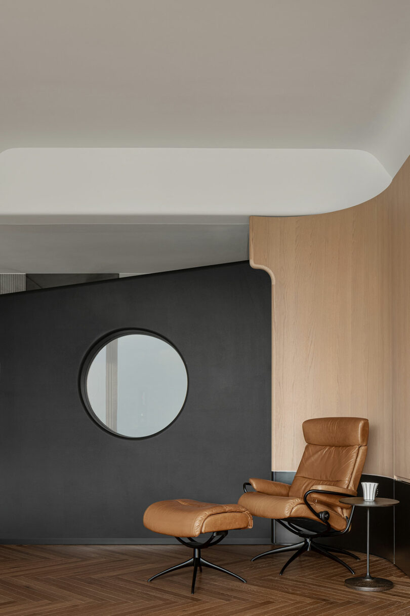 A modern living space featuring a brown leather recliner with a matching ottoman, situated against a dark accent wall with a round window, and a wood panel wall.