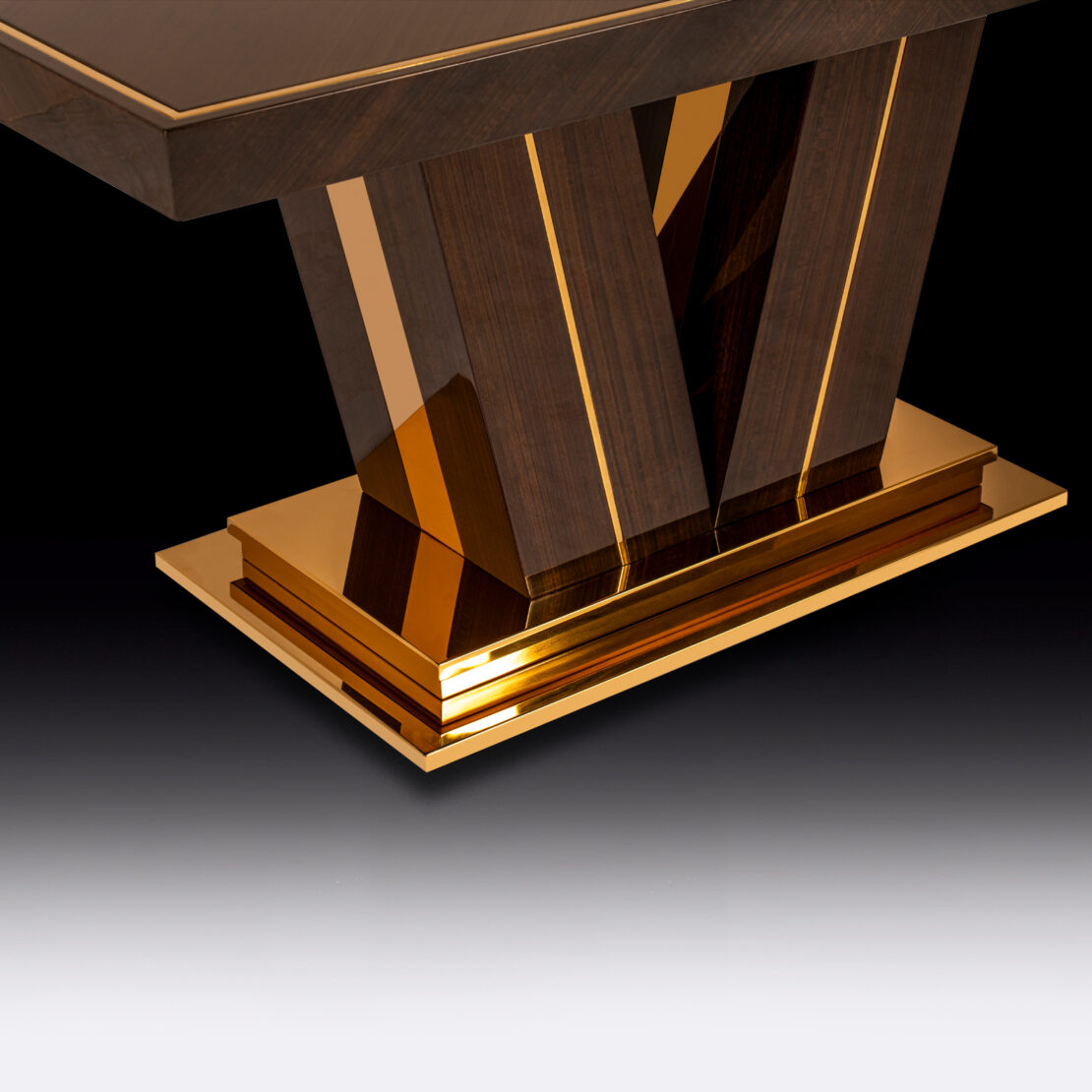 A close-up view of the Exclusive Abstract Rectangular Designer Dining Table with a glossy gold base. The legs form an elegant V-shape design, accentuated by the reflective gold trim, creating a modern and luxurious appearance. The background fades from dark to light, highlighting the table's designer details.