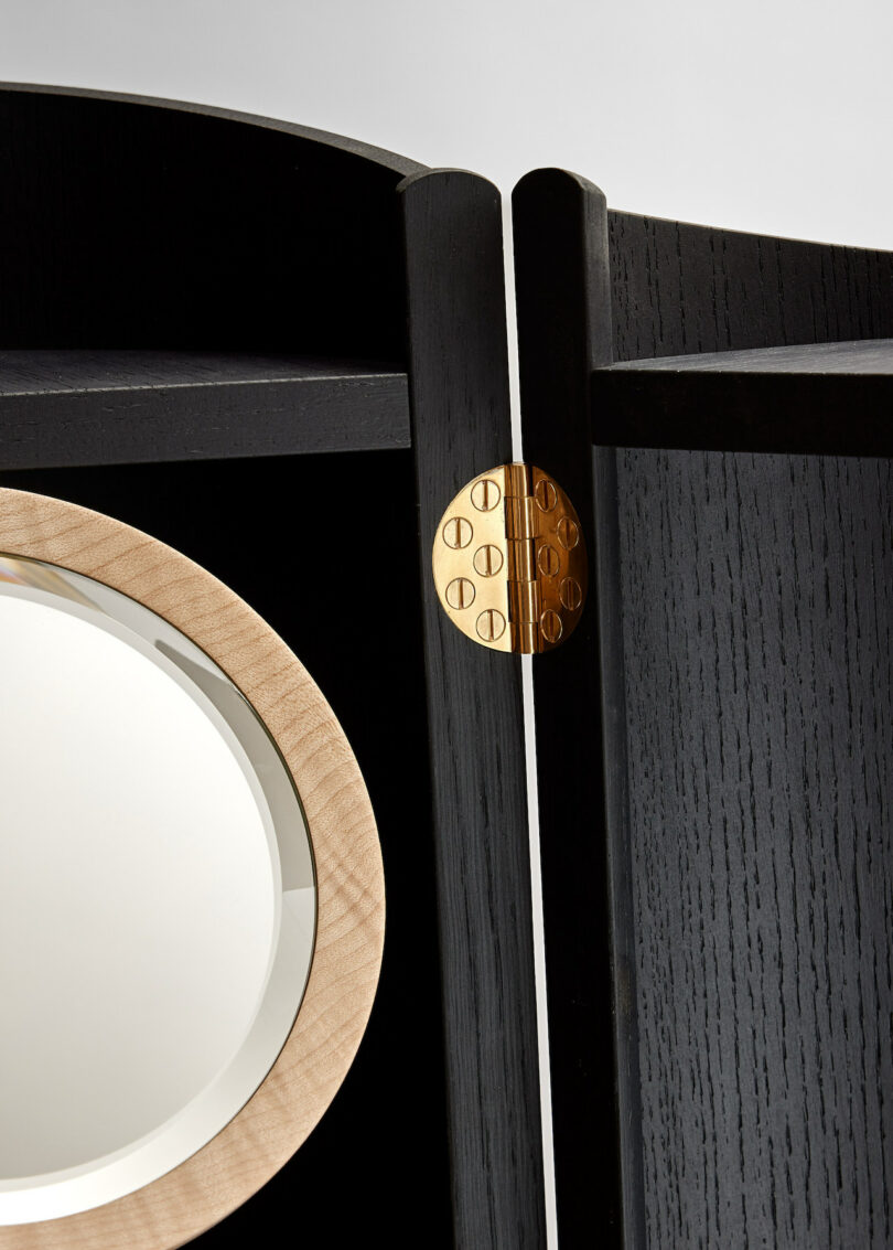 Close-up of a wooden panel with a circular mirror and a brass hinge.