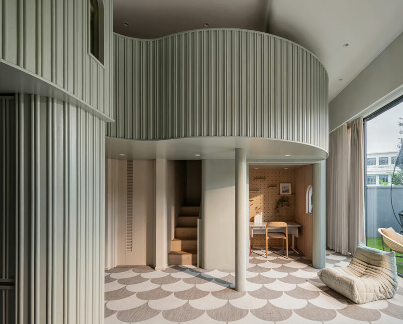 Modern interior room featuring curved walls, geometric patterned flooring, a small staircase, a desk with a chair, and a large window with curtains allowing natural light to enter.