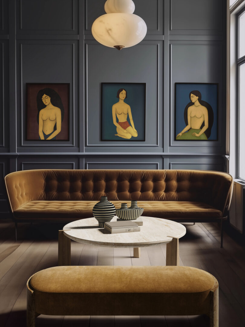 Elegant living room with dark paneled walls, three framed portraits, a brown velvet sofa, a round marble coffee table with vases, and a matching bench. A large window and pendant light complete the scene