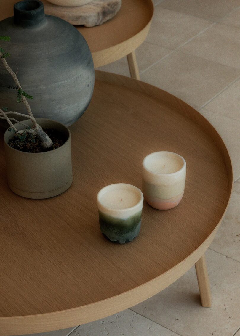 two of OWIU Goods' candles in Forest and Rose Quartz on a circular, wood table next to decorative vases