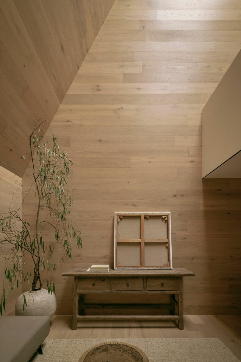 Minimalist interior with wooden walls, a potted plant, a rustic table, and a framed picture facing backward.