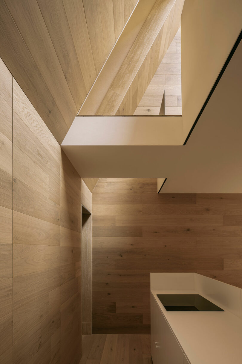 Interior of a modern space with wood-paneled walls and ceiling, featuring a white countertop with a built-in sink. Geometric angles create a minimalist and spacious design.