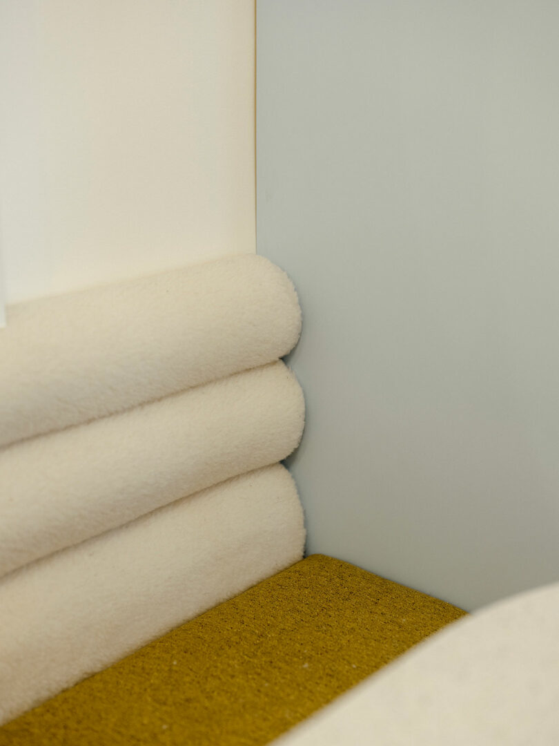 Corner of a room with beige rolled cushions and a mustard-colored carpet.