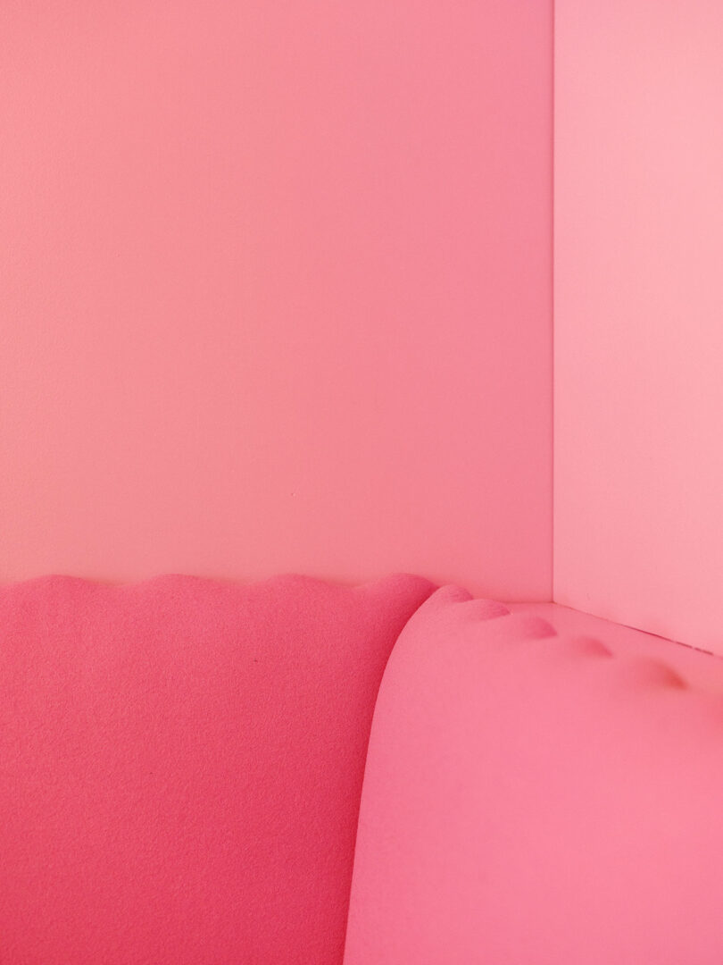 A close-up of a pink upholstered sofa against a corner of two pink walls.