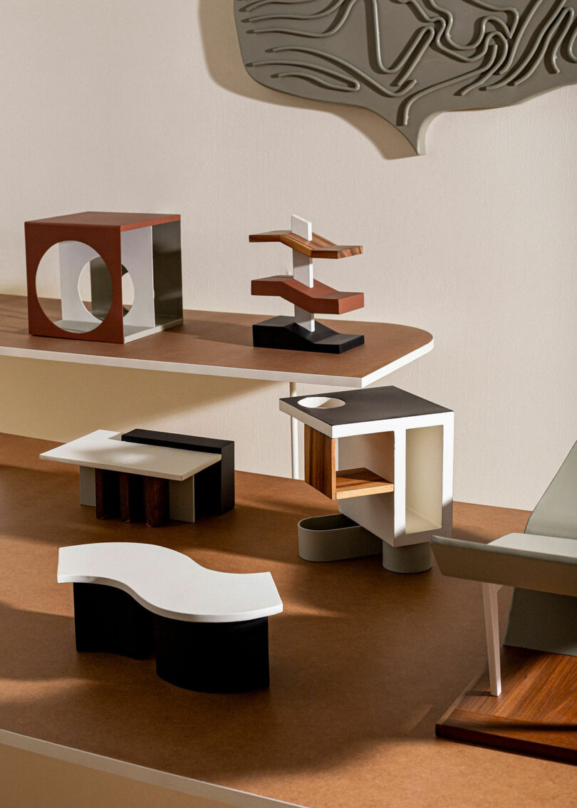 A display of abstract architectural models, featuring various shapes and structures, is arranged on multi-tiered wooden shelves