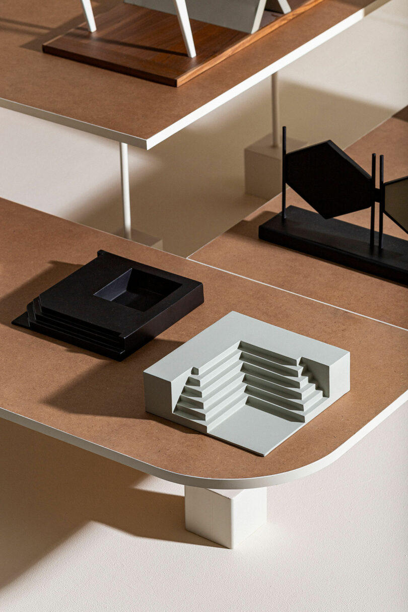 A display of architectural models featuring geometric designs, including a stepped staircase, on a multi-tiered wooden shelf