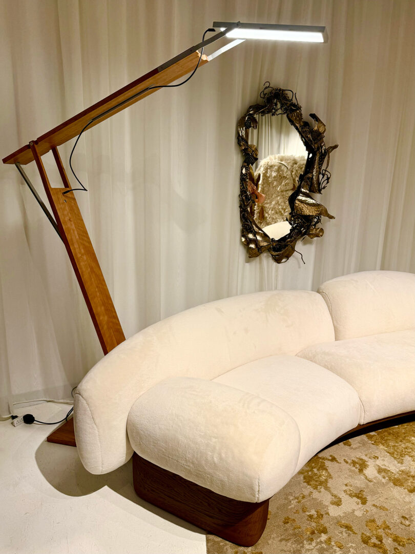 Modern living room with a curved white sofa, a tall wooden floor lamp, and an ornate mirror on the wall.