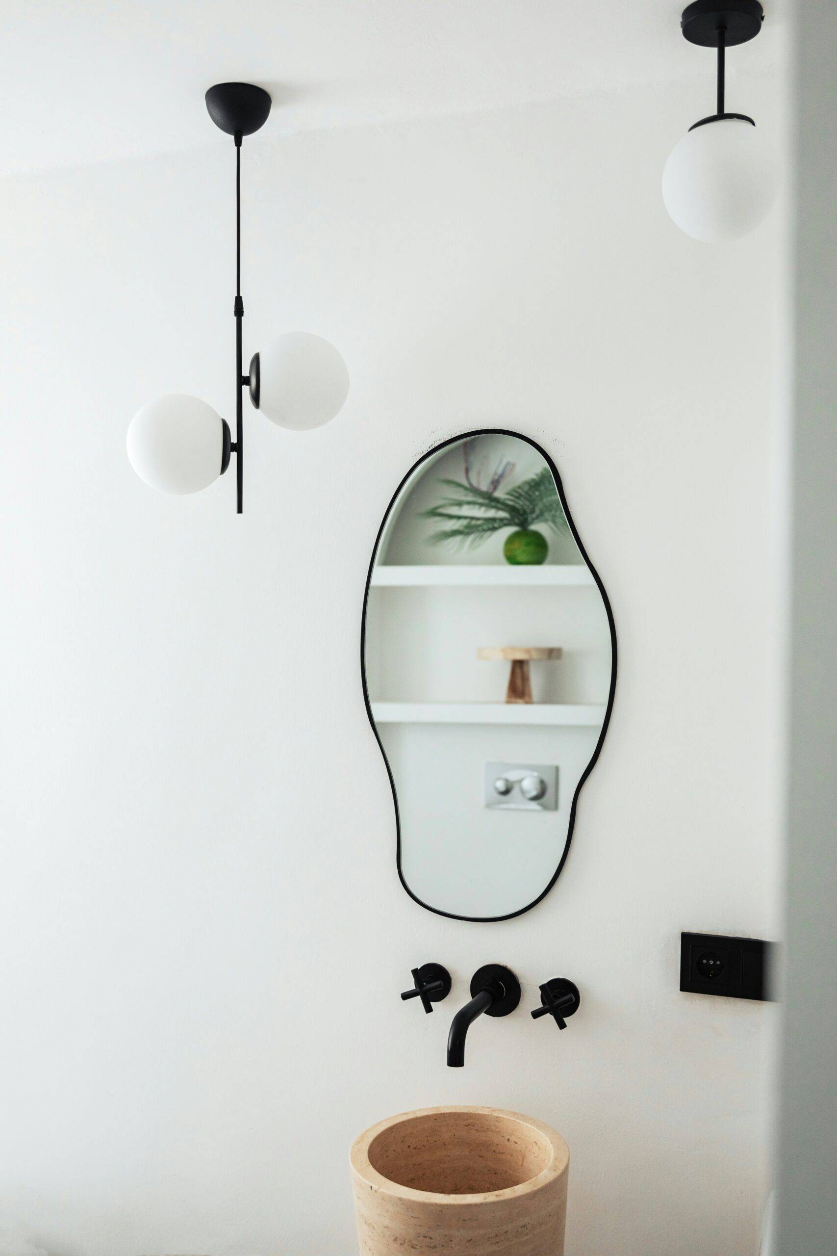 An uneven oval shaped mirror above a small, modern sink in a bathroom.