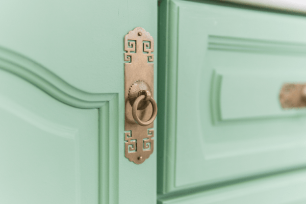 A closeup of a fancy gold drawer pull on a mint green cabinet door.