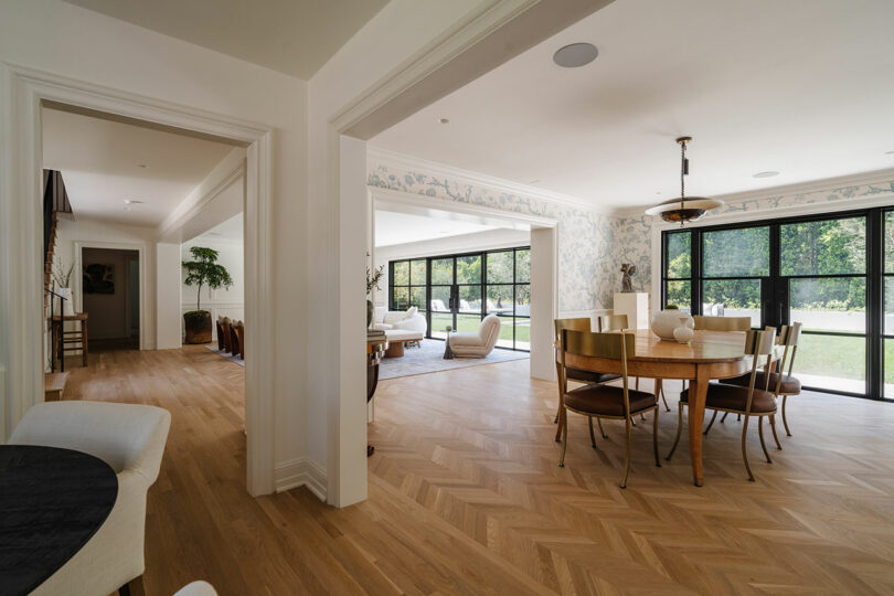 Spacious open-plan dining and living area with wood flooring, large windows, and a view of a lush garden.