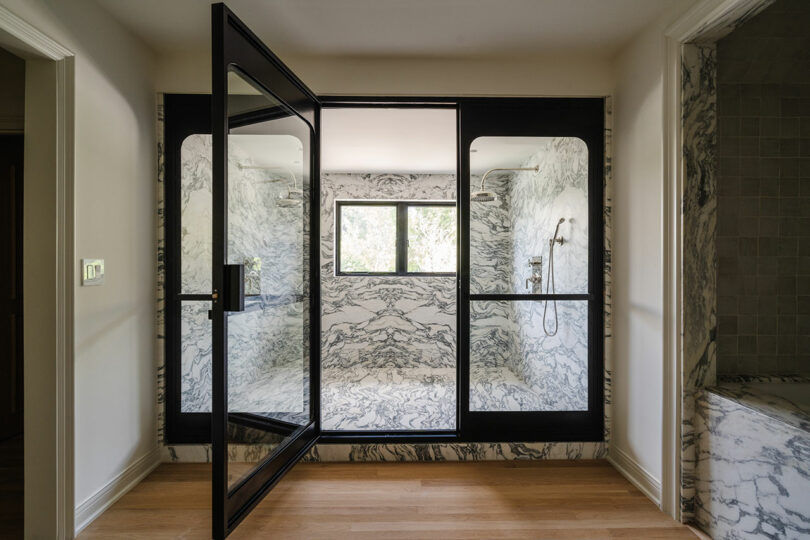 Luxurious bathroom with marble walls and ceiling, a large glass shower door, and a small window overlooking the serene Rose garden.