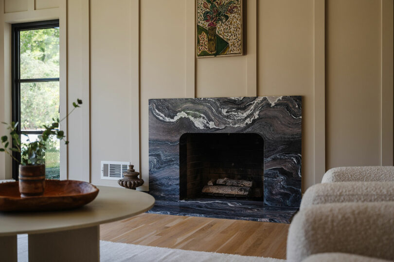 Modern living room with a marble fireplace, light wood flooring, and a round table adorned with decorative items.