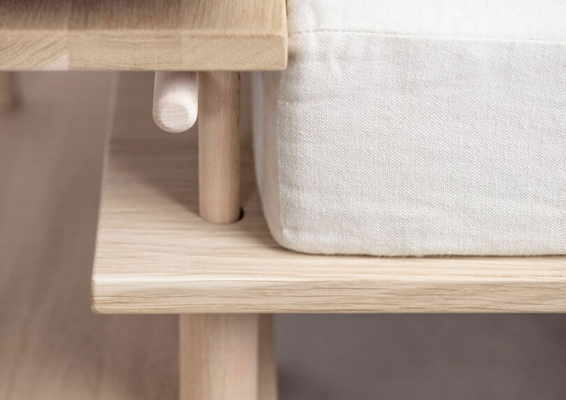 Close-up of a wooden bench with a light-colored cushion. The image highlights the bench's natural wood grain and simple, minimalist design