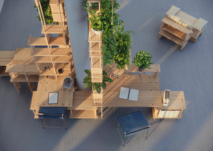 Overhead view of a modular wooden desk system with plants, open books, stools, and a small lounge area with a cushioned seat