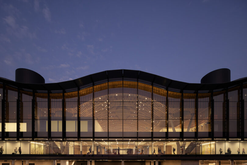 Nighttime view of a modern ZGF-designed building with large glass windows, showcasing interior lighting and silhouetted figures inside.