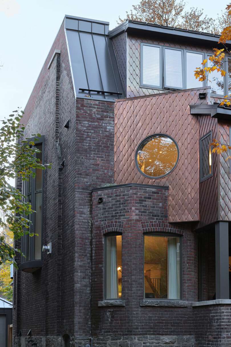 Modern, multi-story brick building with a combination of traditional red bricks and unique copper cladding featuring a circular window and contemporary design elements.