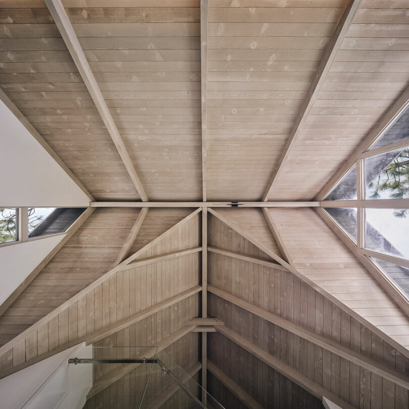 Wooden vaulted ceiling with exposed beams and triangular windows reflecting trees.