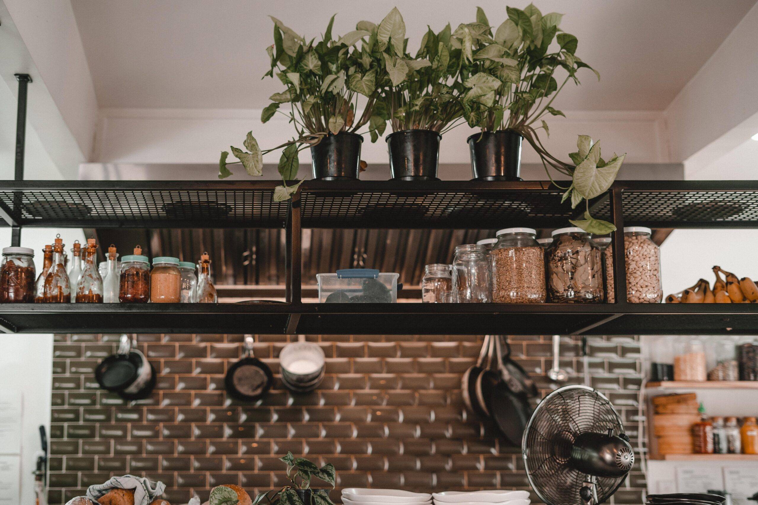 A hanging two tiered metal shelf above a kitchen center island, filled with jars and topped with plants.