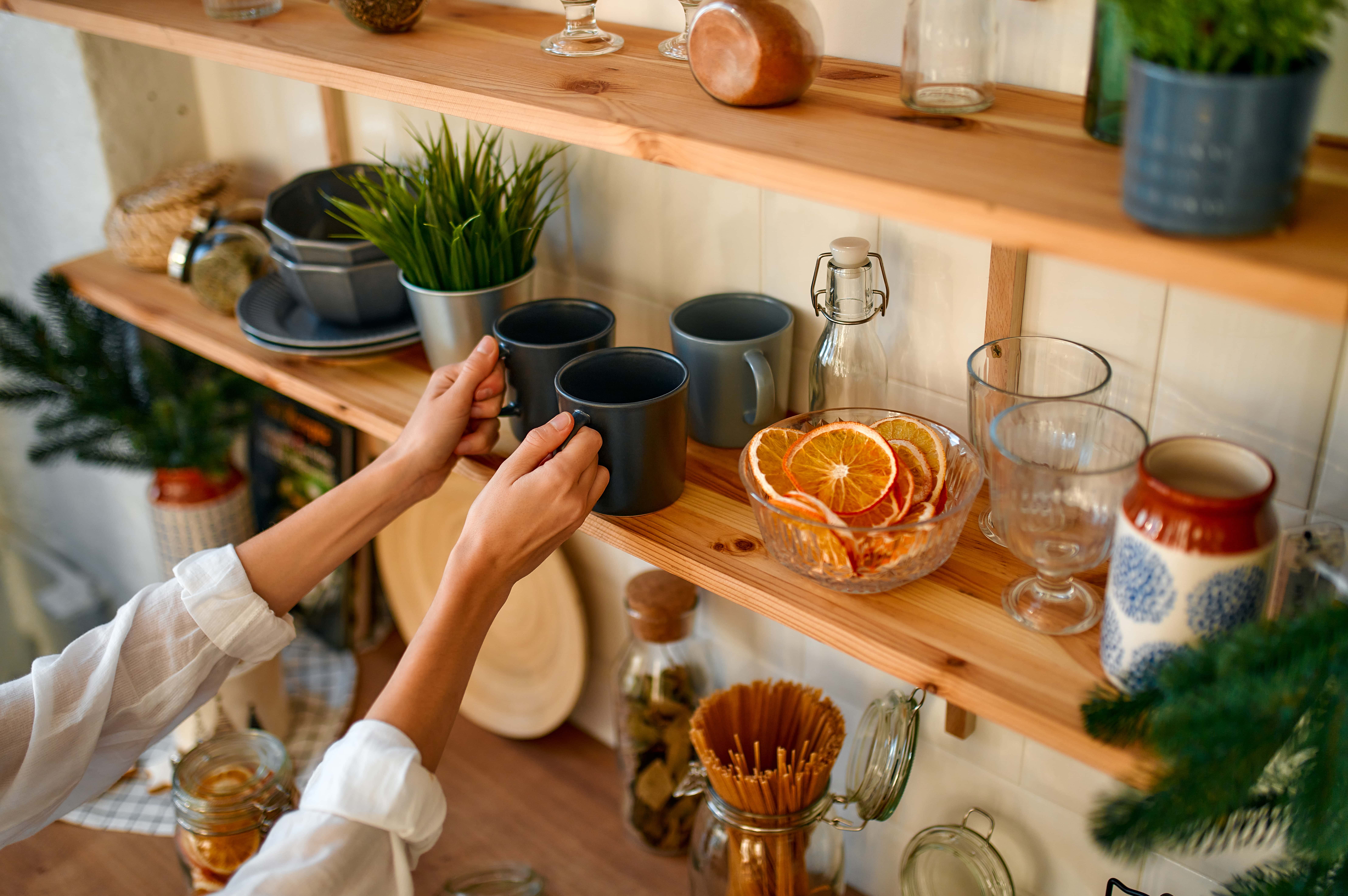 A series of long wall-mounted shelf units filled with mugs, glasses and other decor items, a hair of hands reaching out to grab two mugs.