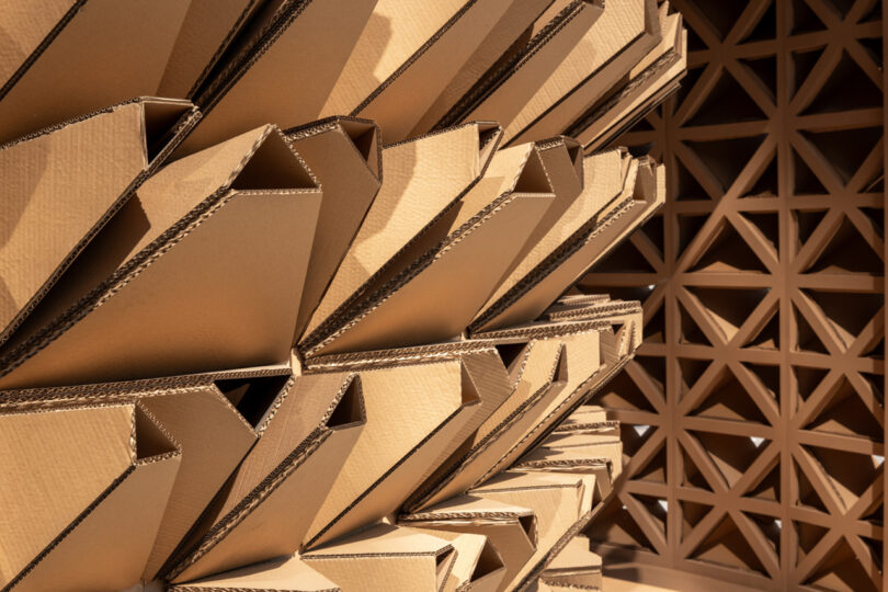 Close-up of a geometric wall made of stacked, open cardboard boxes and a lattice design partition in the background.