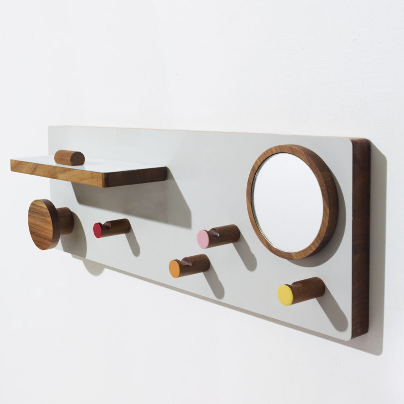 Wall-mounted organizer with wooden pegs, a shelf, and a circular mirror on a white background