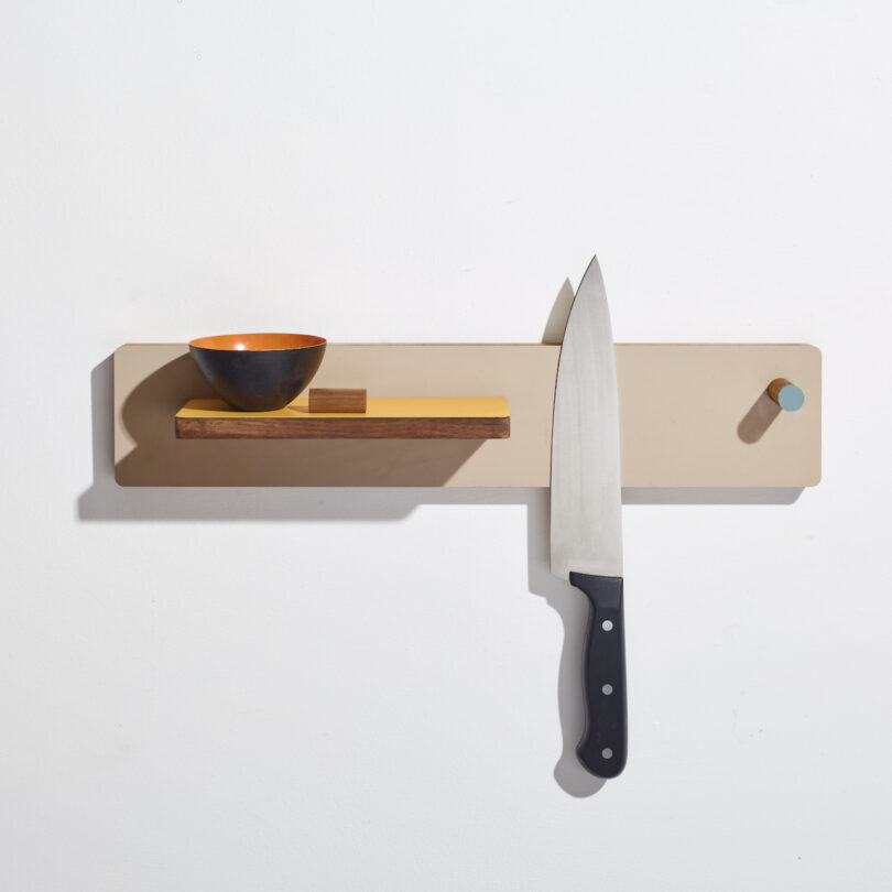 Magnetic wall rack holding a knife, a small bowl, and a wooden block against a white background