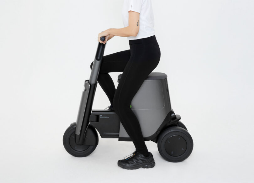 Person sitting on a compact, modern, foldable electric scooter against a plain background