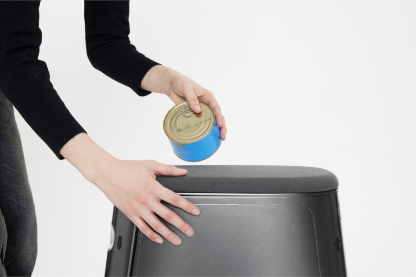 A person places a can on top of a black appliance