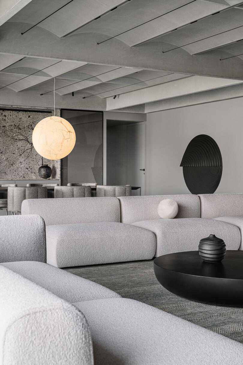 Modern living room with minimalist design, featuring grey sofas, a circular coffee table, spherical decor items, and a round pendant light. Walls are adorned with abstract art.