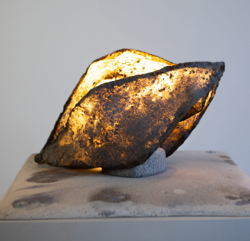 A glowing, roughly-shaped stone sculpture sits on a dusty pedestal, illuminated from within