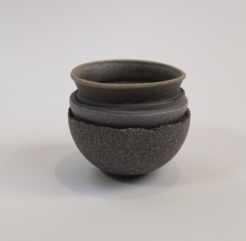 A small, round, dark gray ceramic bowl with a textured surface and smooth rim, placed on a plain white background